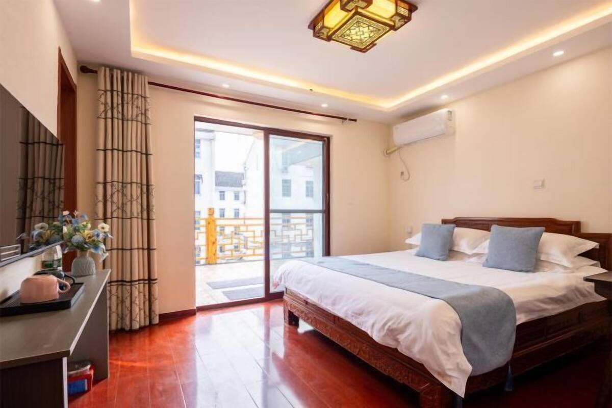 A hotel room with a bed, a desk, a lamp, and a view of the outside.