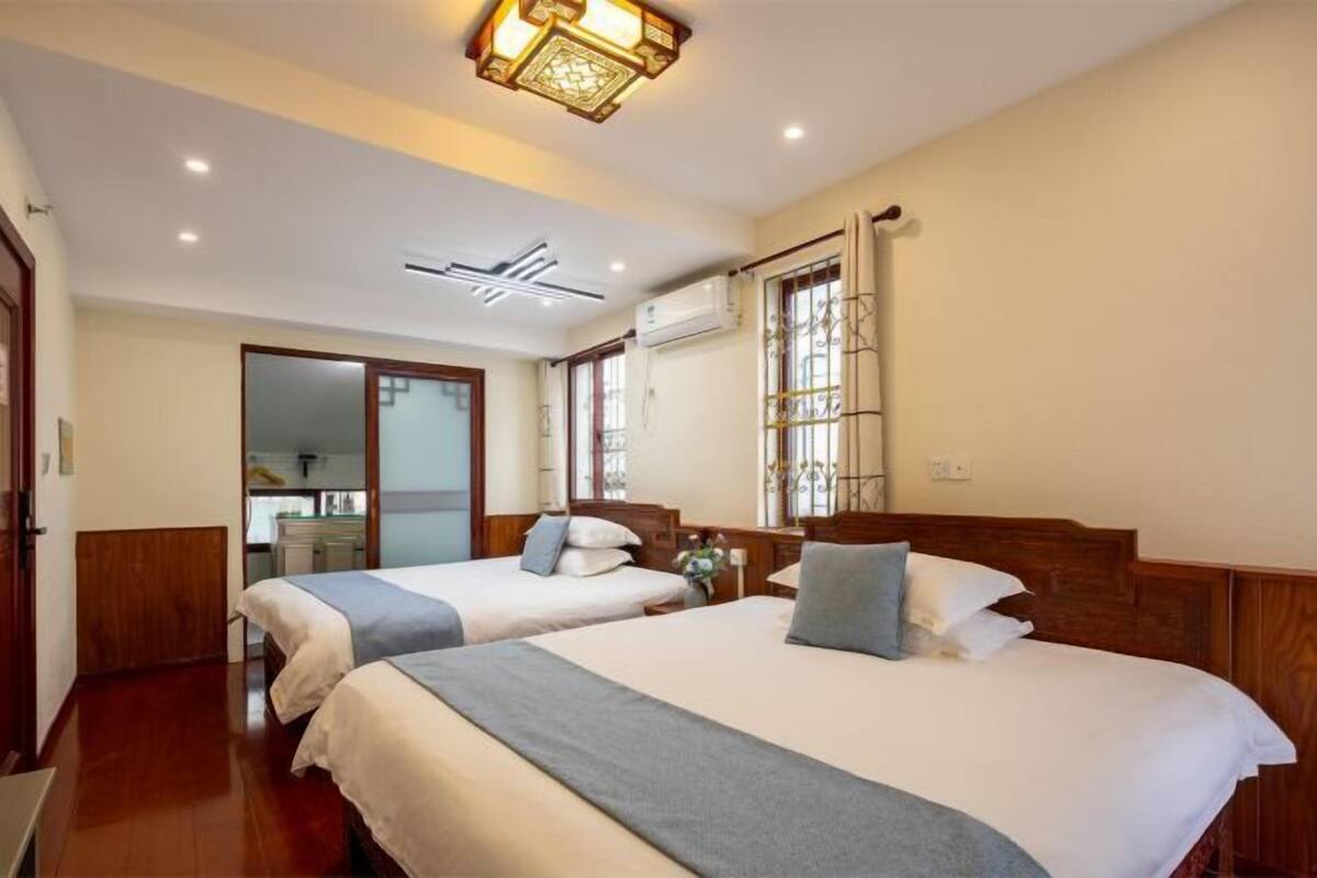 A hotel room with two beds, a wooden headboard, a ceiling light fixture, and a window with a view.