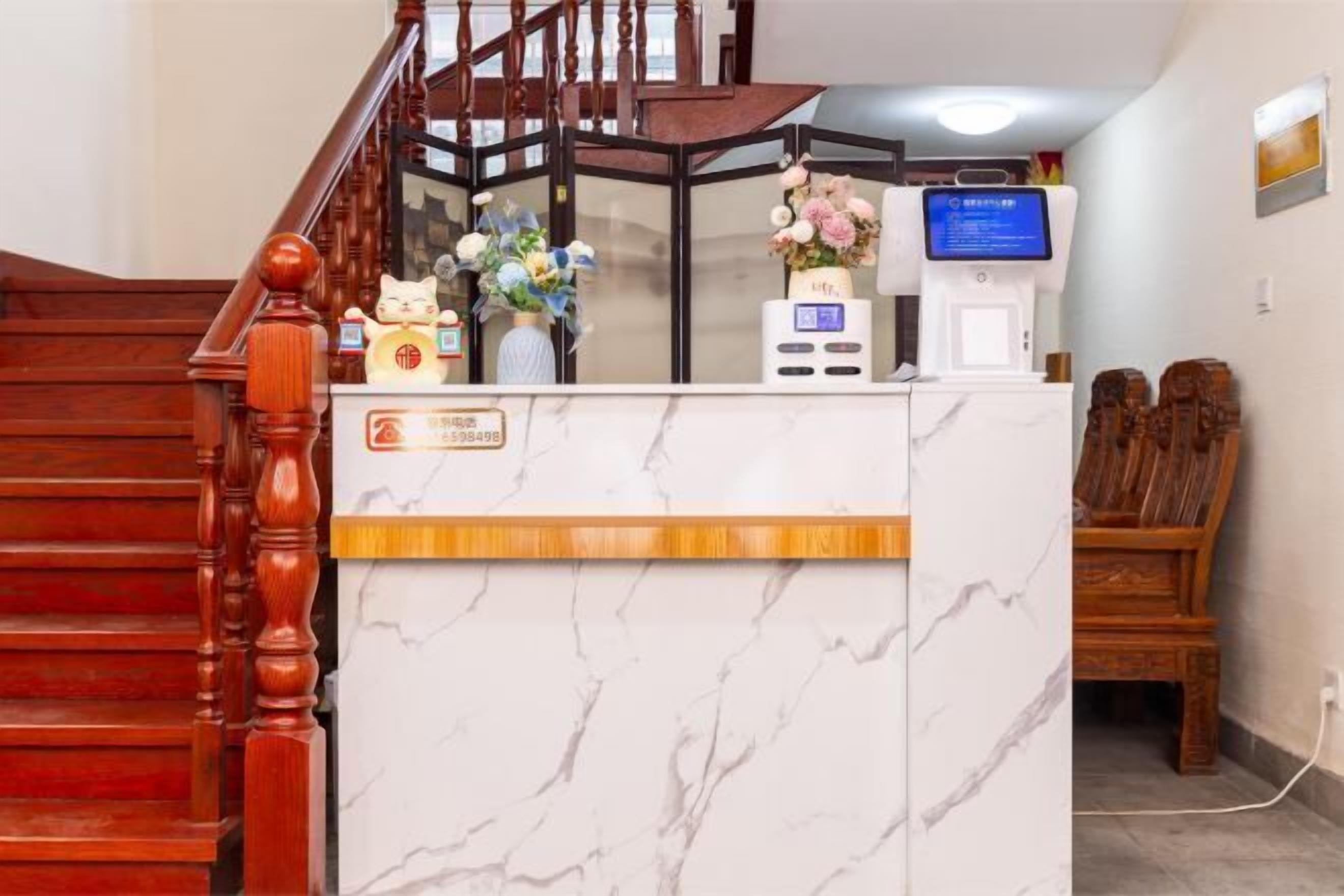 A reception desk with a marble top, a wooden staircase, and a digital display.