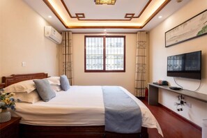 Habitación de hotel con una cama, televisión, ventana e iluminación empotrada en el techo.