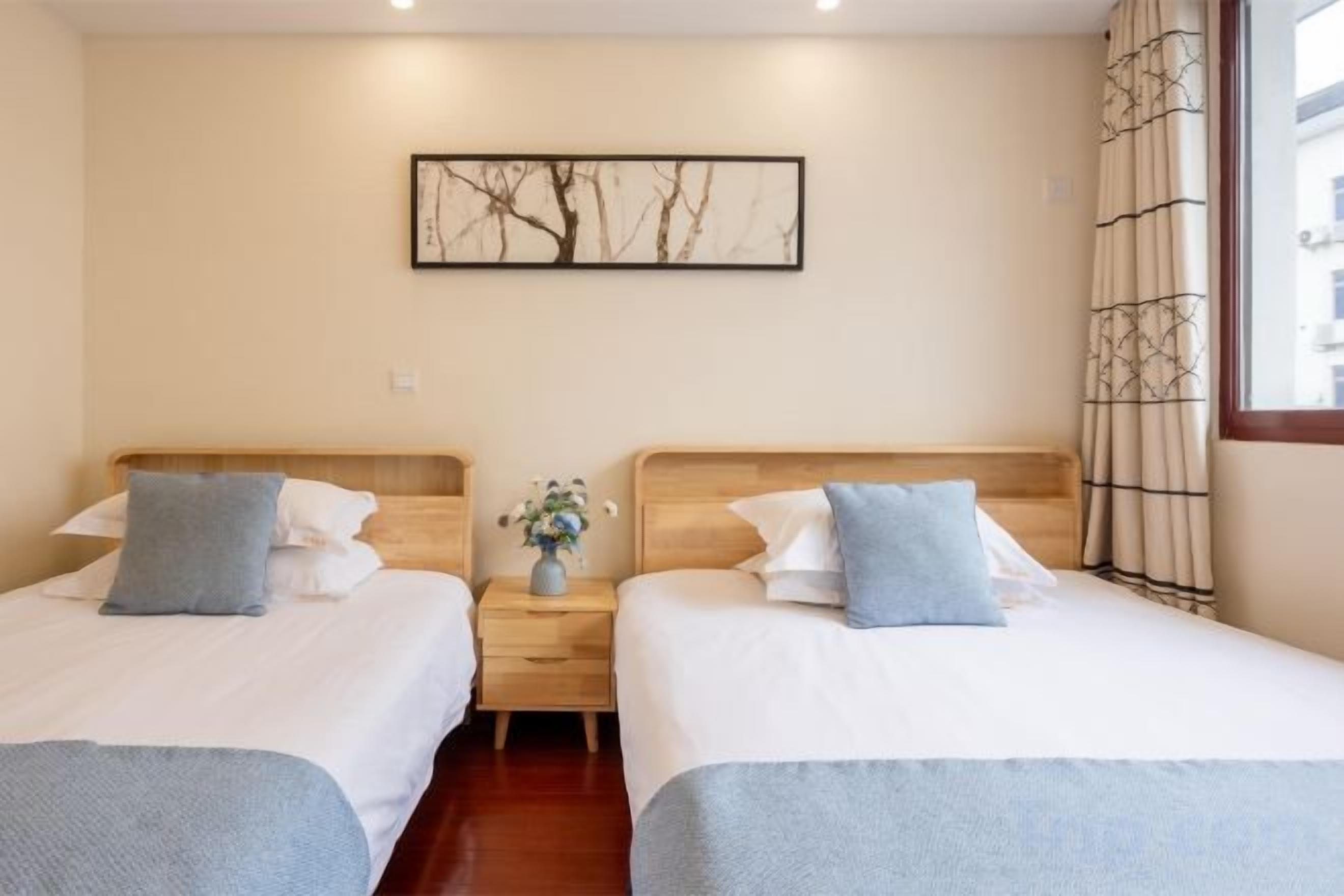 Une chambre d’hôtel avec deux lits, une table de chevet, un vase avec des fleurs et un tableau encadré au mur.