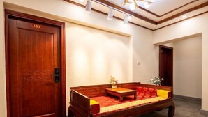 A hotel room with a wooden door labeled "303", a sofa with a red and yellow patterned cover, and a small table with a vase of flowers. - Zhouzhuang Hefeng Xiyu Inn (Kunshan)
