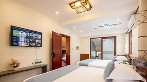 A hotel room with two beds, a TV mounted on the wall, a desk with a vase of flowers, and a mirror. - Zhouzhuang Hefeng Xiyu Inn (Kunshan)