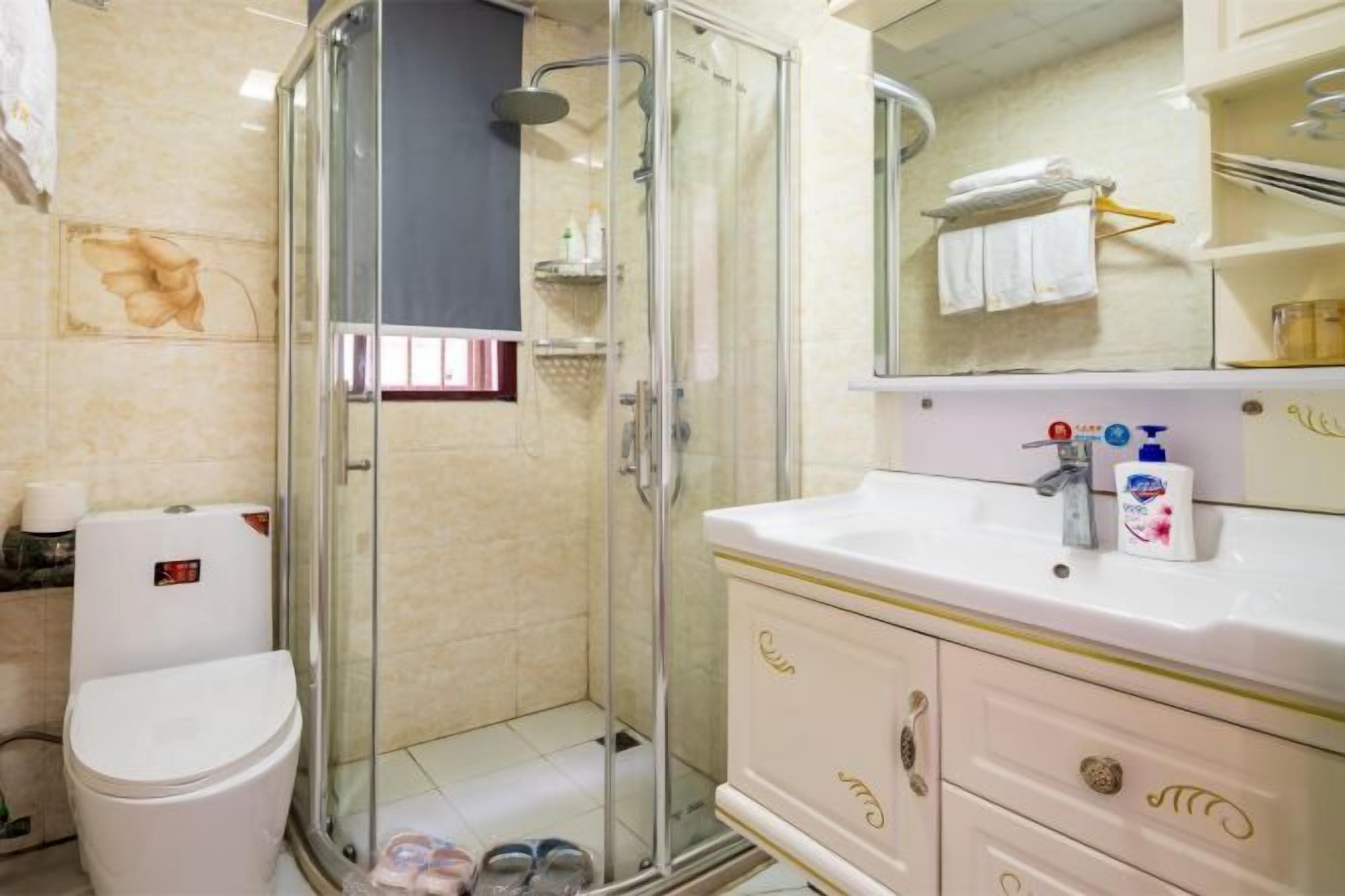A bathroom with a glass-enclosed shower, a white toilet, and a vanity with a mirror and toiletries.