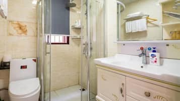 A bathroom with a glass-enclosed shower, a white toilet, and a vanity with a mirror and toiletries.