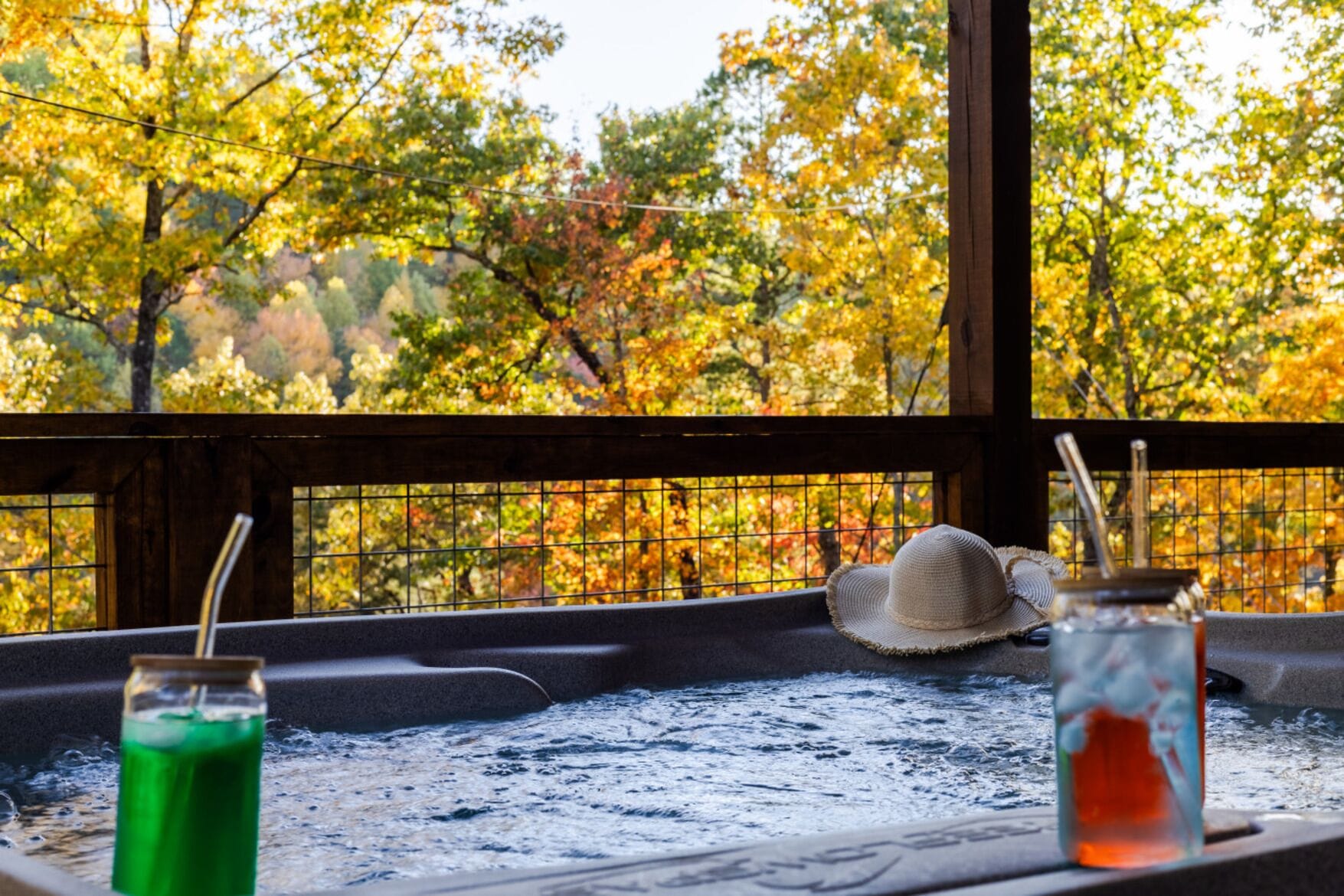 A hot tub with a view of autumn trees, a straw in a glass, and a straw in a jar.