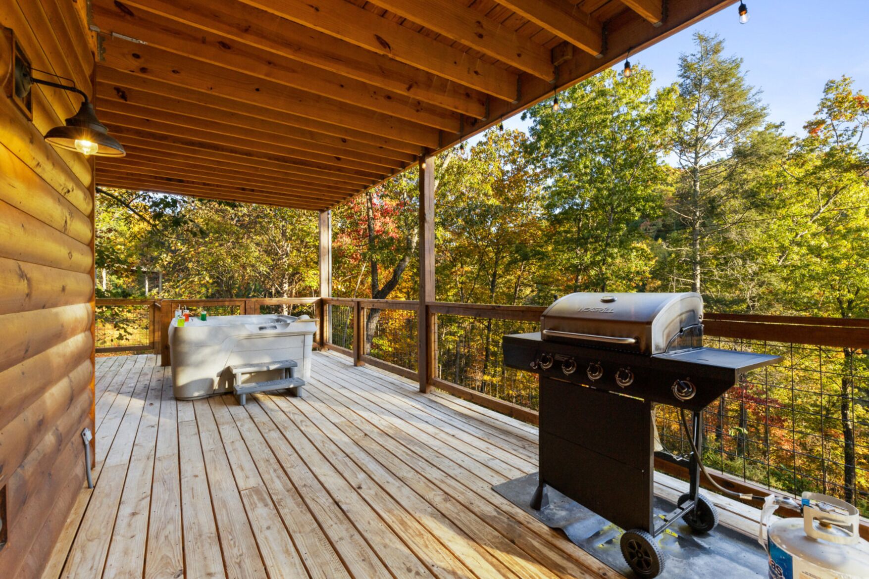 A wooden deck with a hot tub and a grill, surrounded by trees.