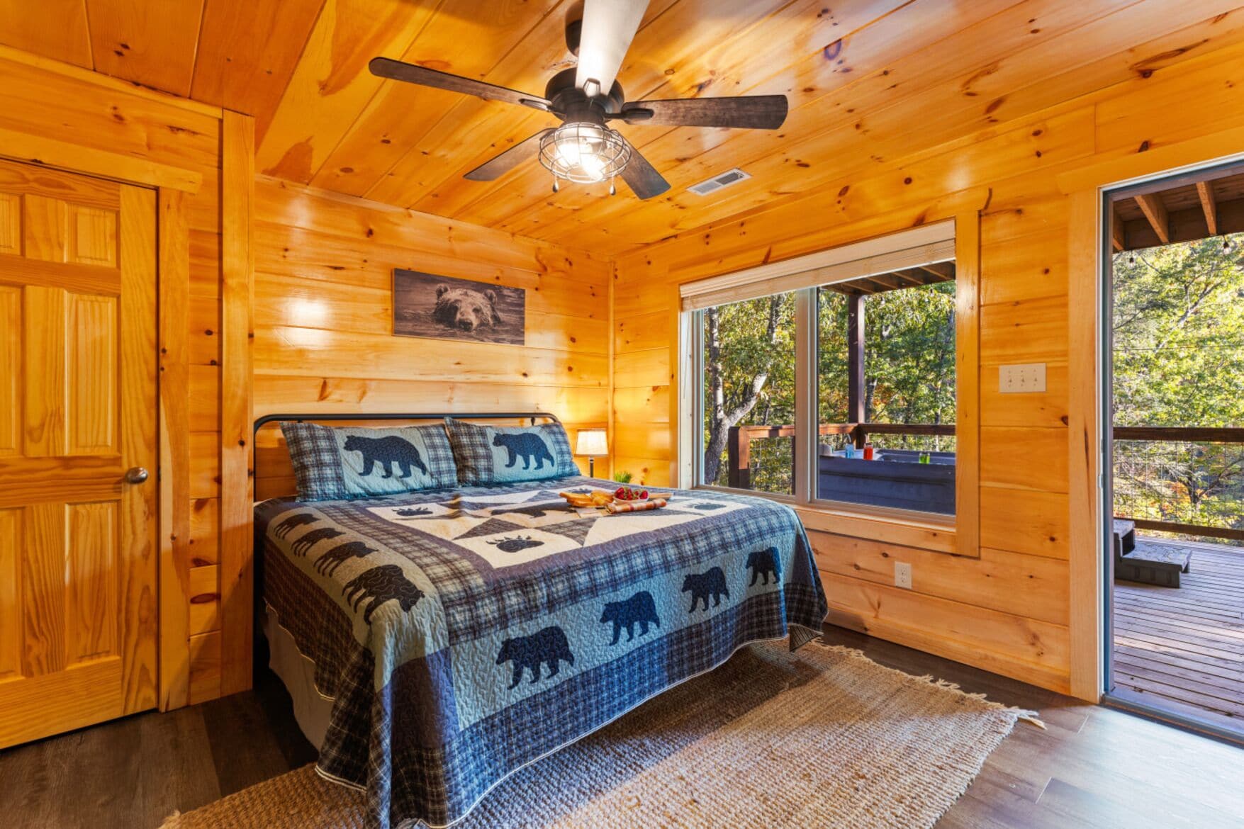 A wooden cabin bedroom with a bed, a ceiling fan, a window, and a door.