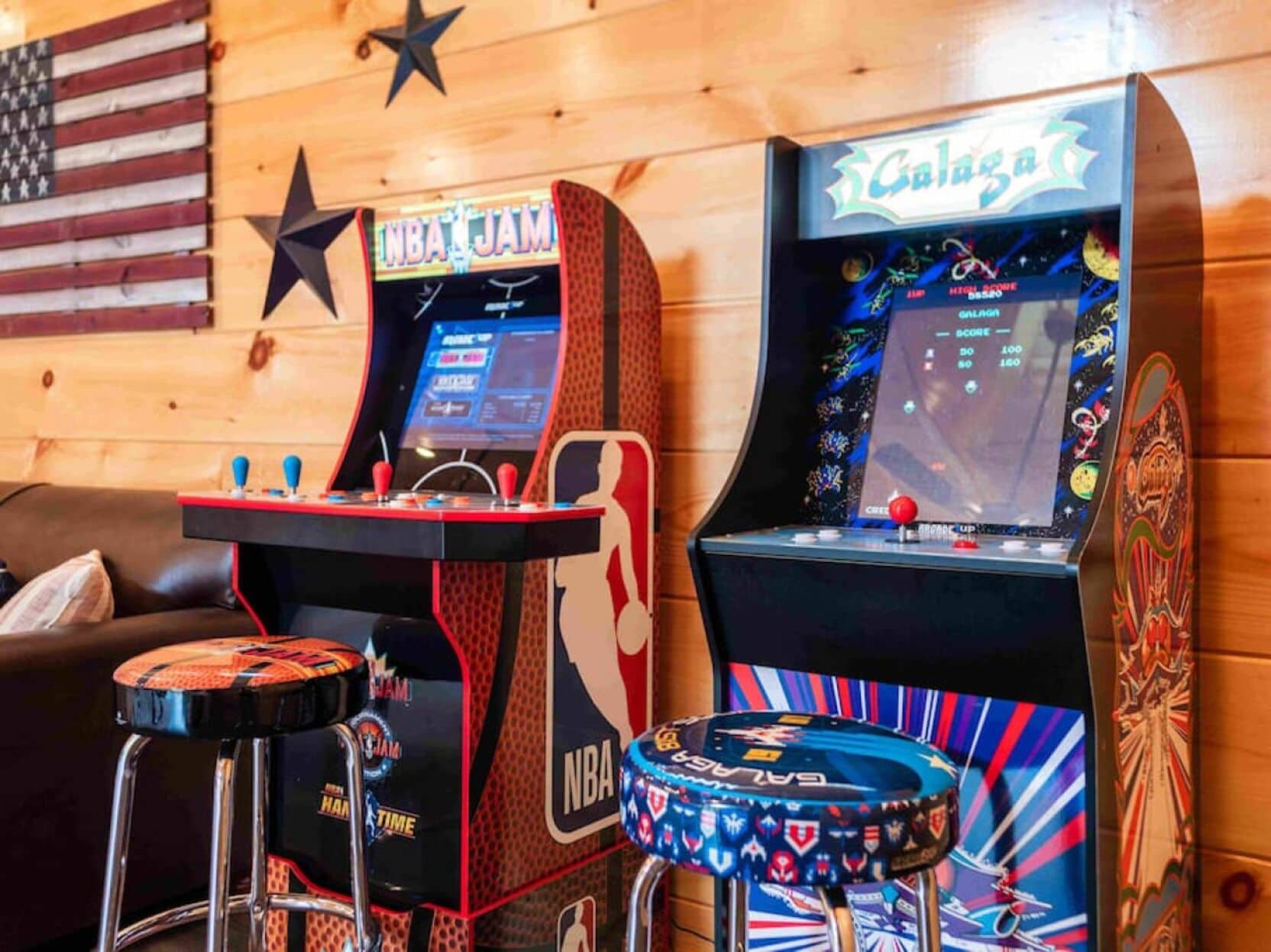 Two arcade machines with NBA JAM and Galaga themes, a star decoration on the wall, and a wooden panel background.