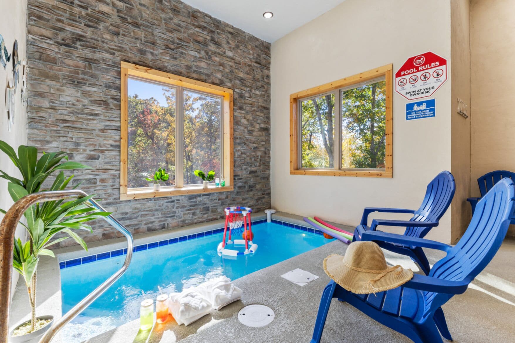 A pool area with stone walls, two windows, and blue chairs.