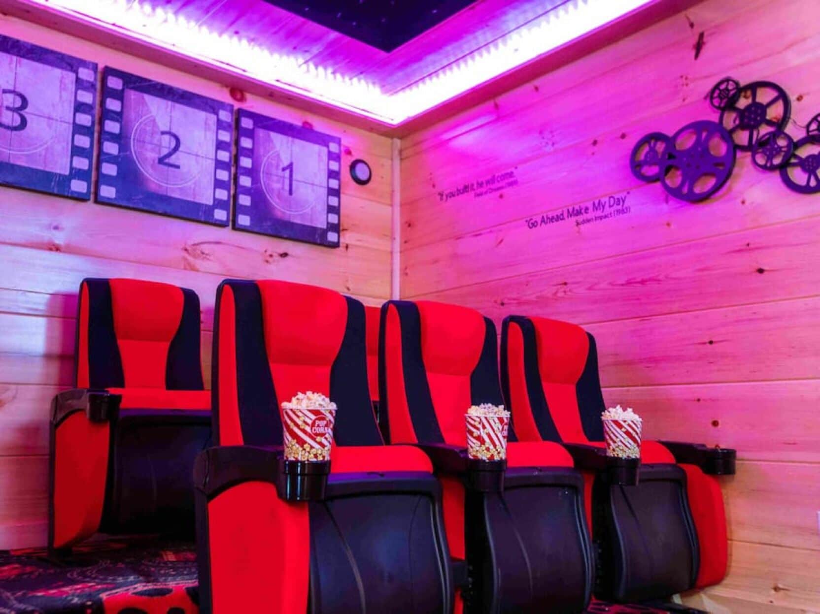 A row of red and black cinema-style seats with popcorn containers, wooden panel walls, and a filmstrip decoration on the wall.