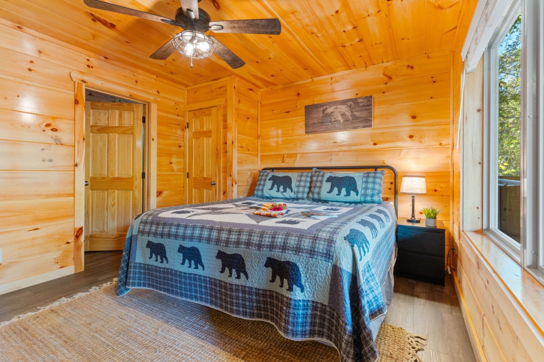 Une chambre dans une cabane en bois, avec un lit, un ventilateur de plafond, une fenêtre et une porte.