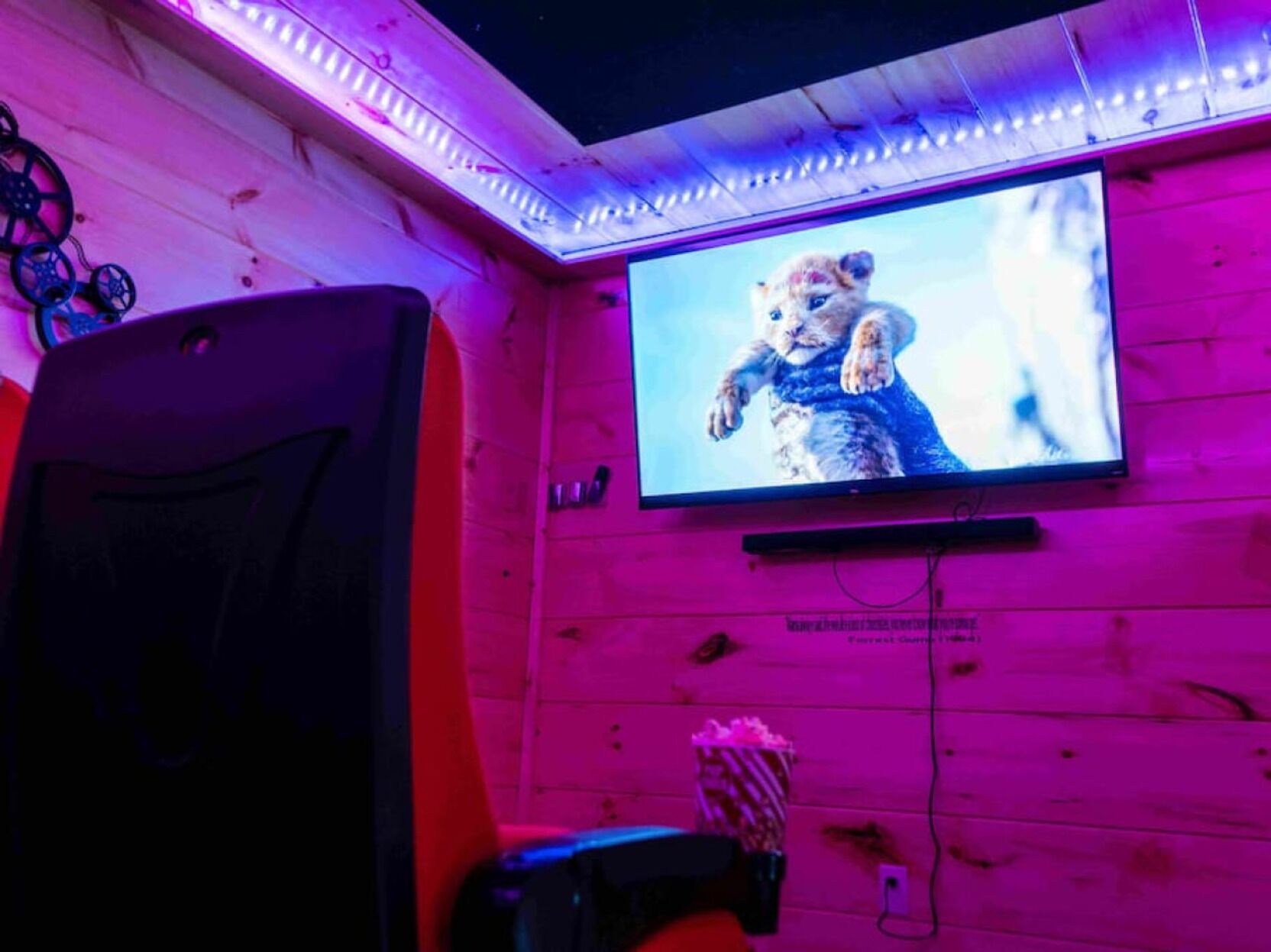 A room with a large flat-screen TV mounted on a wooden wall, a gaming chair, and a popcorn bucket.