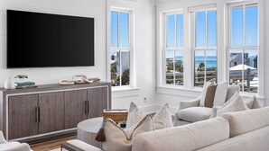 A living room with a large flat-screen TV, a gray sofa, and a wooden cabinet. - Expansive Designer Home with Gulf Views, One Min to Beach, Private Pool, LSV (Santa Rosa Beach)