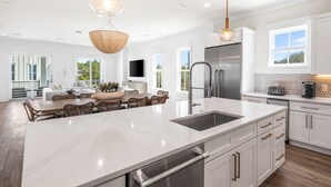 A modern kitchen with a large island, stainless steel appliances, and a dining area with a view. - Expansive Designer Home with Gulf Views, One Min to Beach, Private Pool, LSV (Santa Rosa Beach)