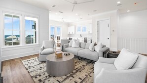 A spacious living room with a large gray sectional sofa, a round coffee table, and a view of the ocean through large windows.