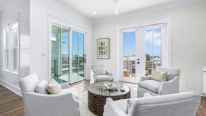 A spacious living room with a glass sliding door leading to a balcony, a ceiling fan, and a 'No Wake Zone' sign.