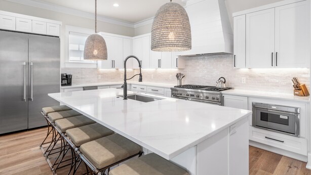 A modern kitchen with white cabinetry, a large island with bar stools, stainless steel appliances, and pendant lighting.