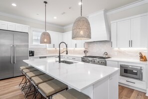 Una cocina moderna con armarios blancos, una isla grande con taburetes de bar, electrodomésticos de acero inoxidable e iluminación colgante.