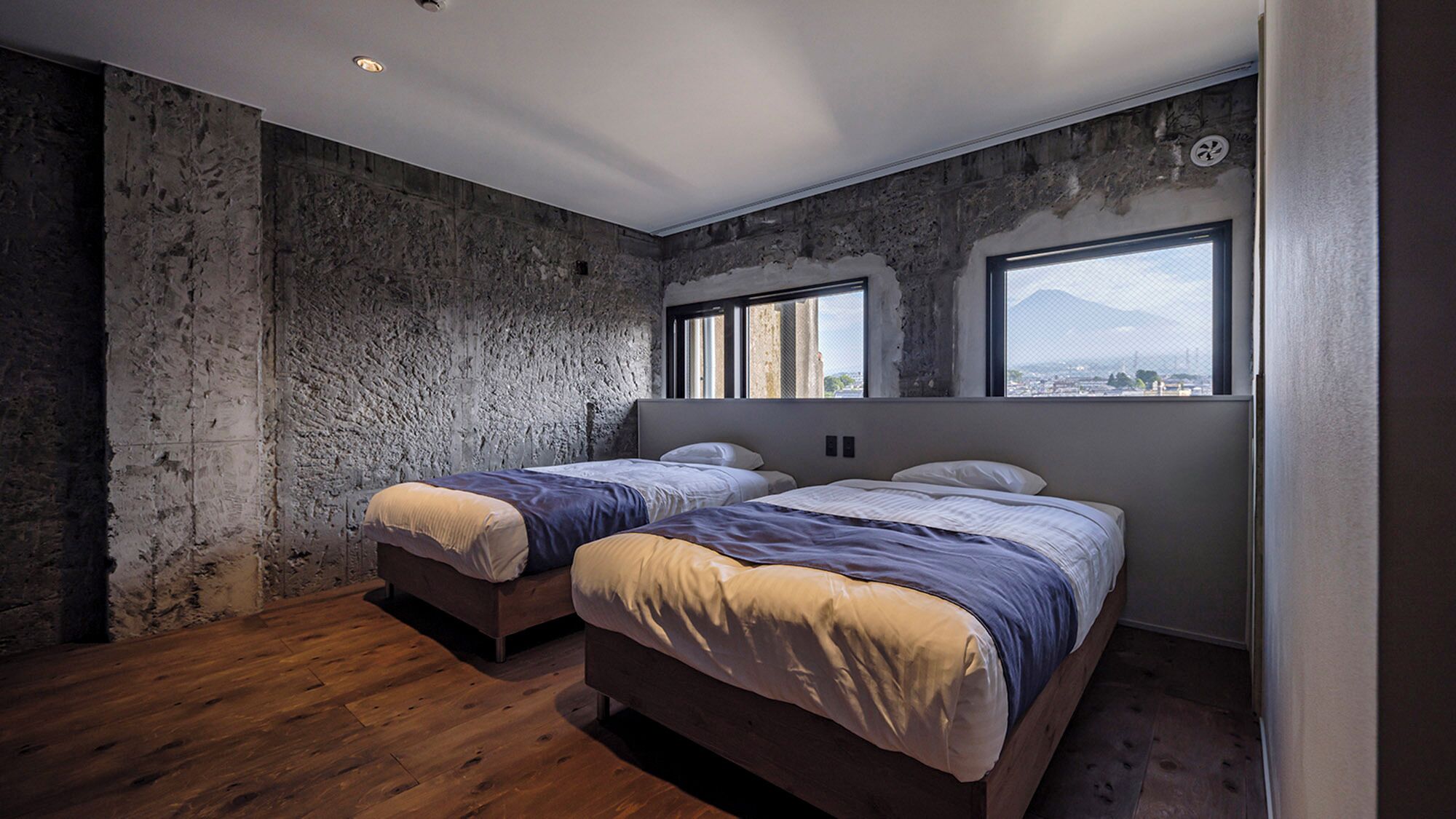 Una habitación con dos camas, un ventanal grande y una pared de piedra.