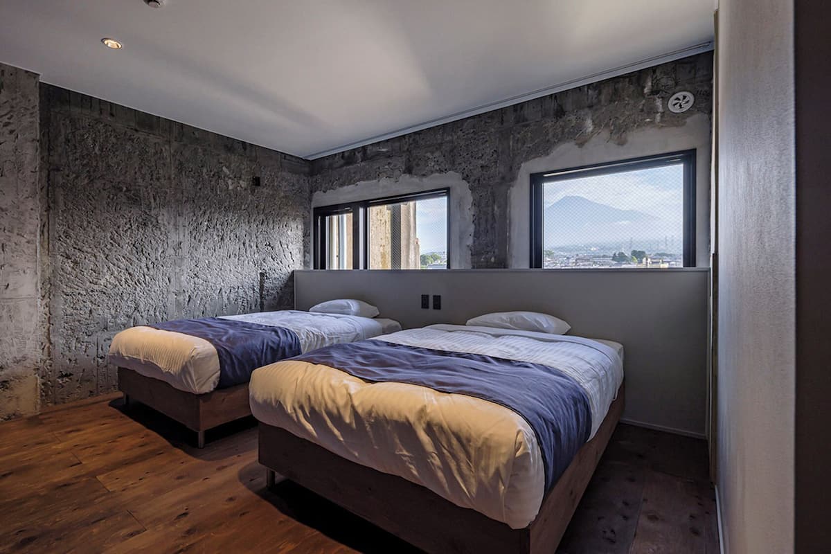 A room with two beds, a large window, and a stone wall.