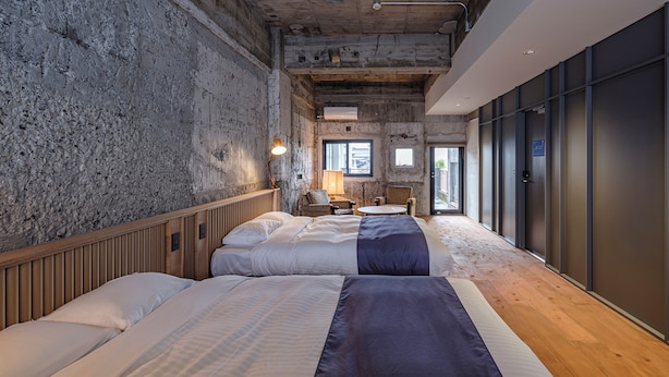 Ein Hotelzimmer mit zwei Betten, Holzboden, Steinwand und einem großen Fenster.