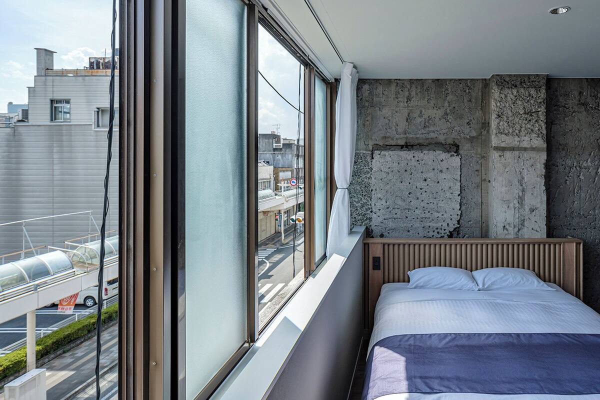 A bedroom with a large window, a concrete wall, and a bed.