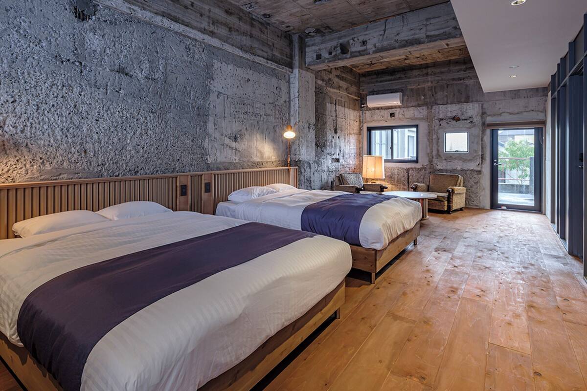 A room with two beds, wooden flooring, and a rustic stone wall.