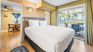 Ein Hotelzimmer mit einem großen Bett, einem Schreibtisch mit Stuhl, einem Deckenventilator und Blick ins Freie durch eine Schiebetür.