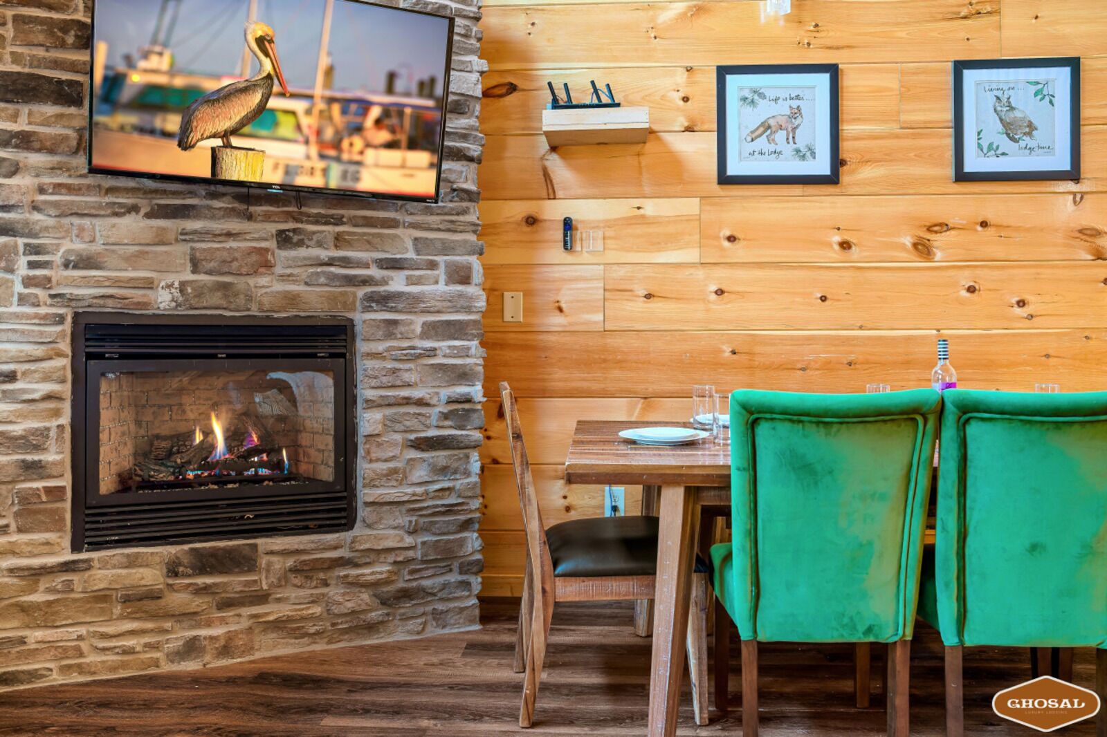 L’intérieur chaleureux d’un chalet avec une cheminée en pierre, des murs en bois, une table à manger avec des chaises et des œuvres d’art encadrées accrochées au mur.
