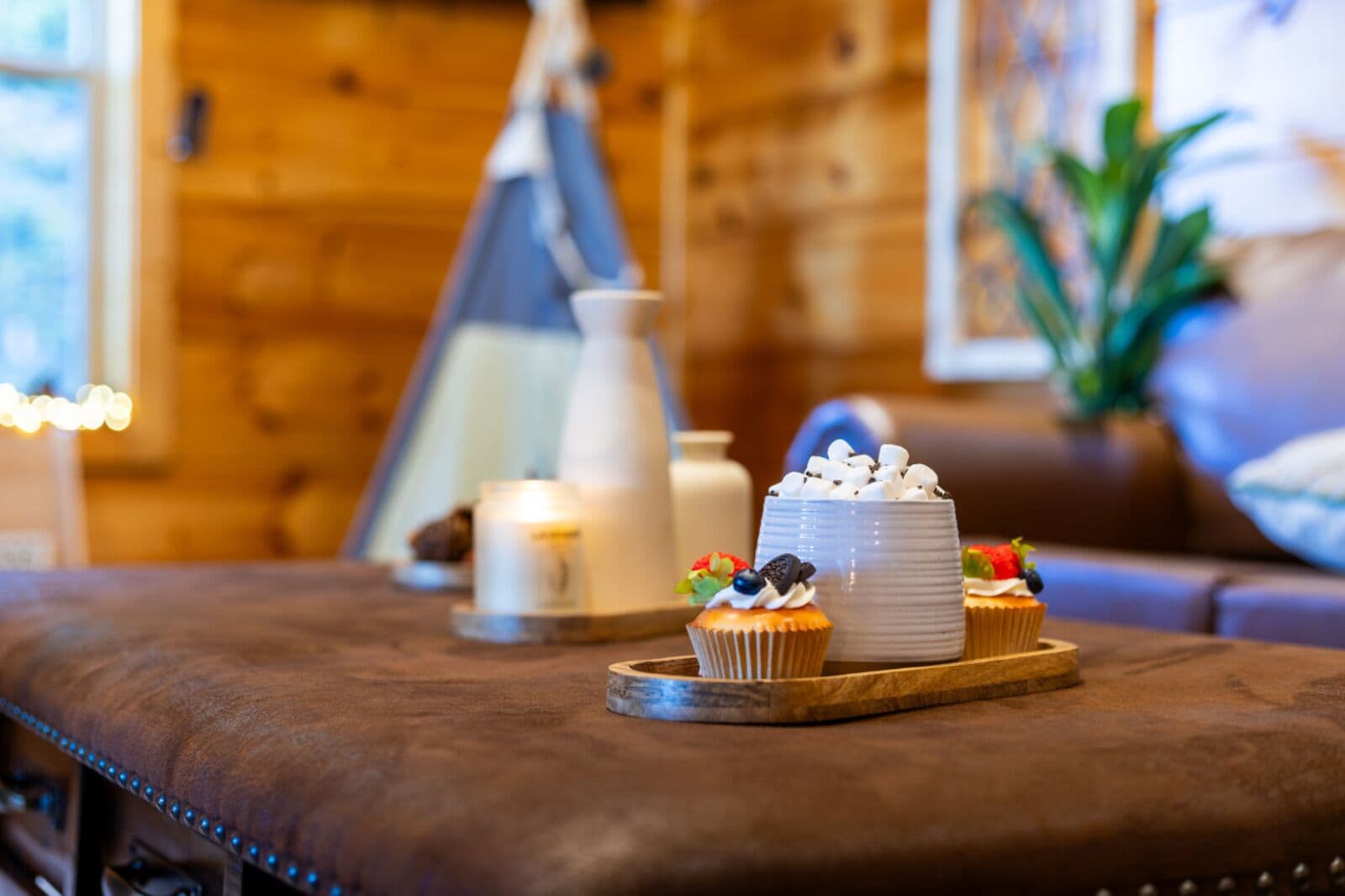 A cozy room with a wooden interior, a cushioned bench, a white cake with marshmallows, and a small cupcake on a wooden tray.