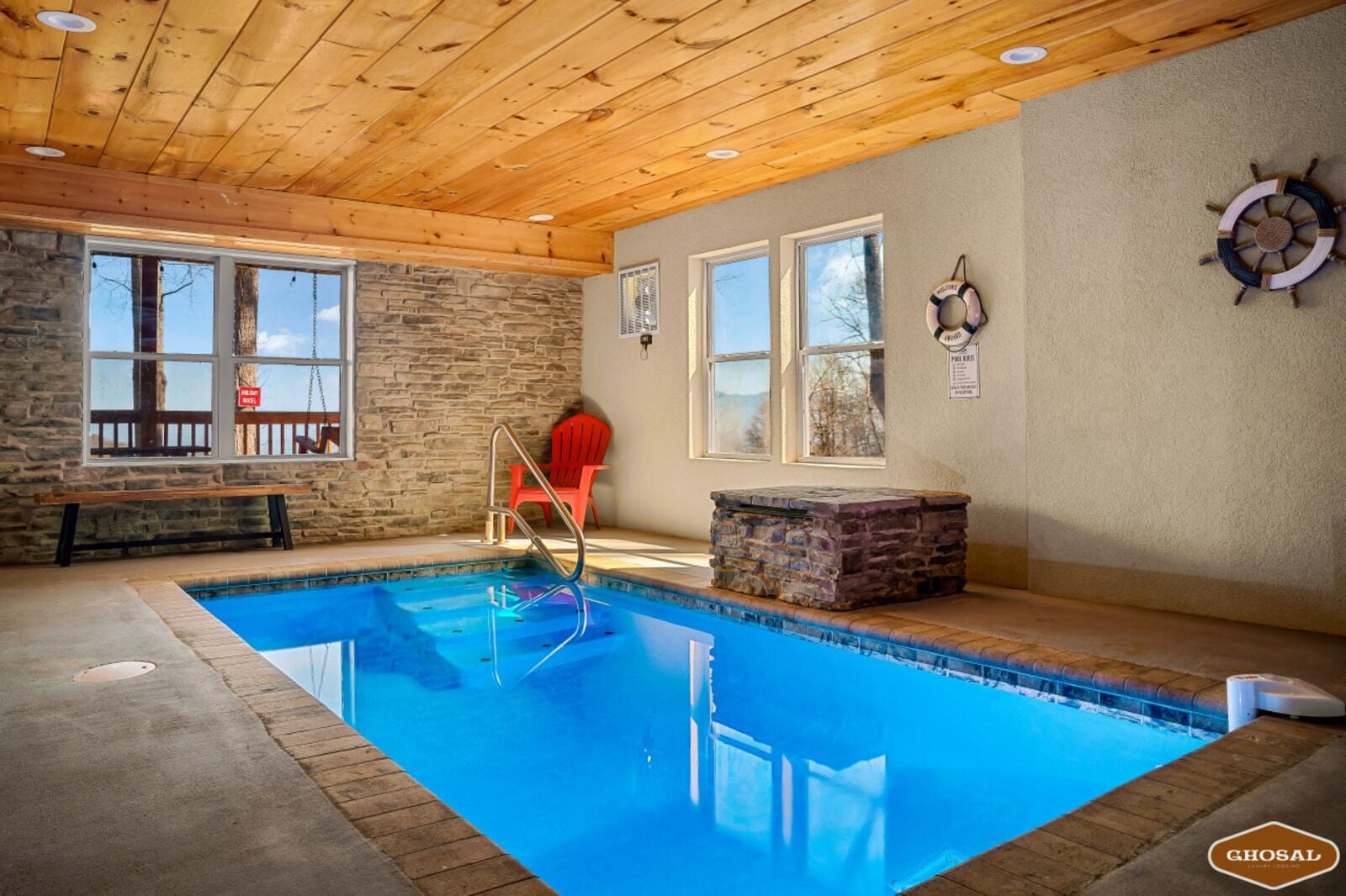 Une piscine intérieure avec des murs en pierre, un plafond en bois et un banc près de la fenêtre.