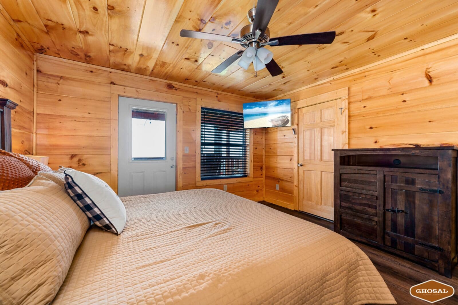 A wooden cabin bedroom with a bed, a ceiling fan, a door, and a window with blinds.