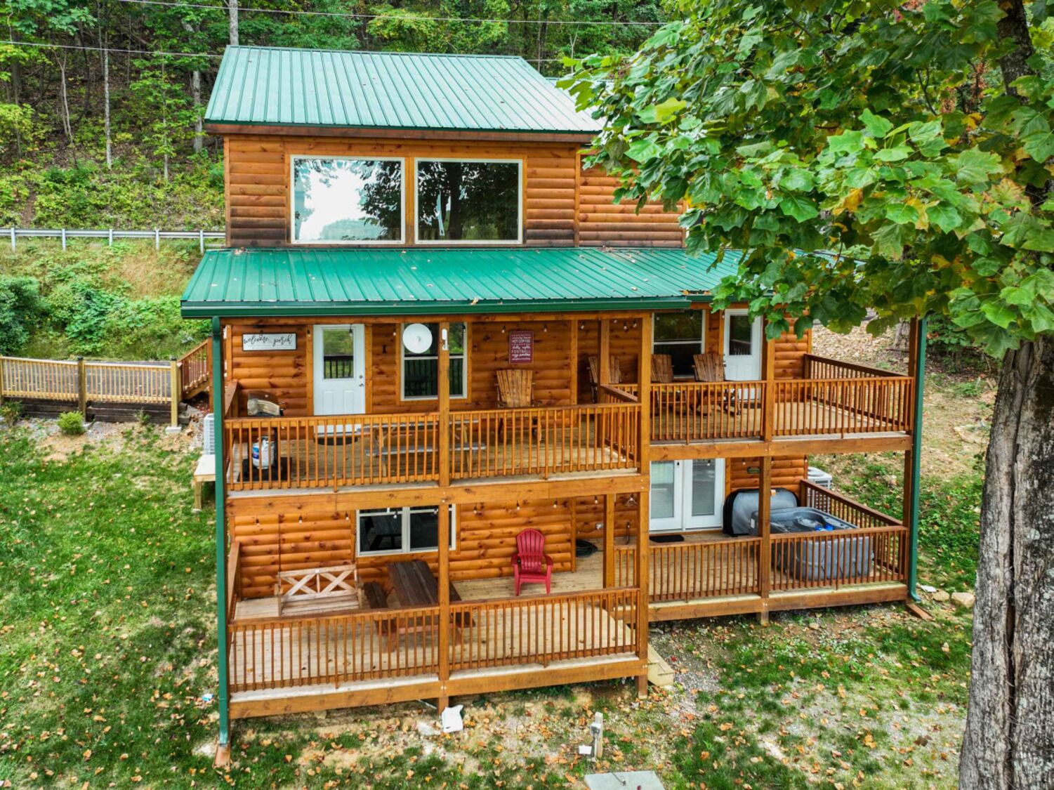 A two-story log cabin with a green roof, multiple balconies, and outdoor seating.
