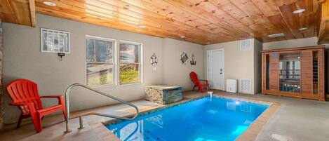 A pool area with a wooden ceiling, two red chairs, a stone feature, and a glass cabinet.