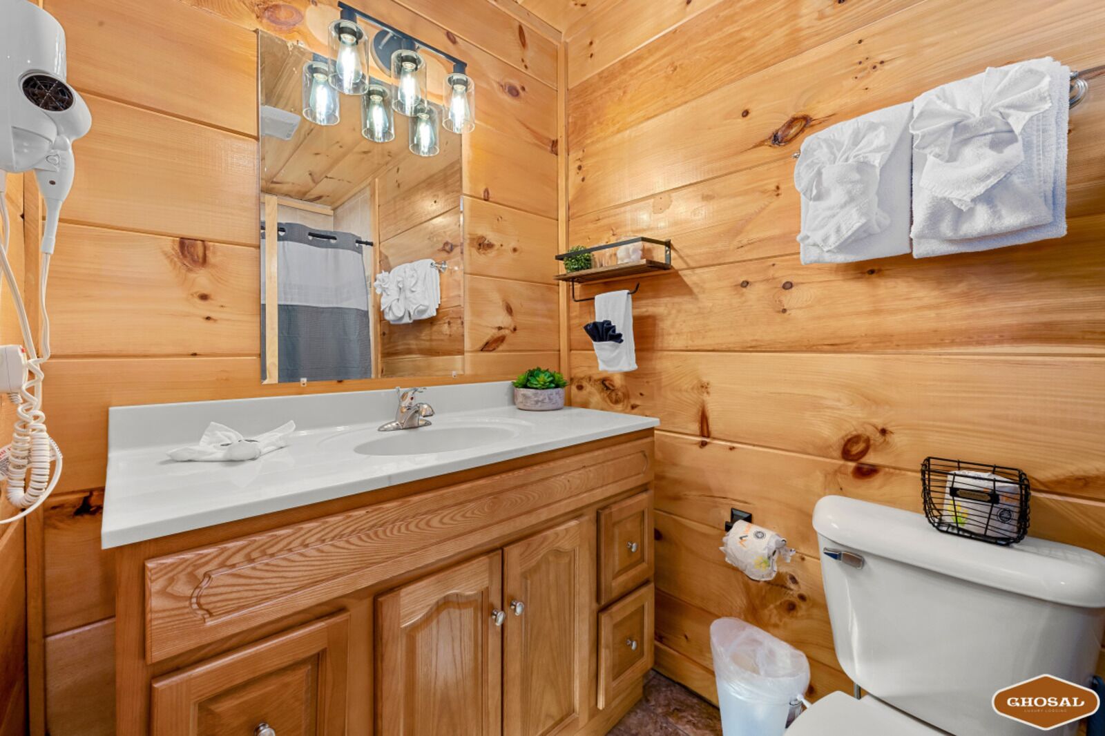 A wooden cabin bathroom with a white sink, wooden cabinets, a mirror, and a toilet.
