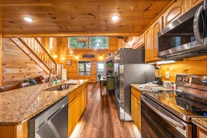 A kitchen with wooden cabinets, granite countertops, stainless steel appliances, and a wooden staircase.