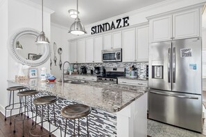 Uma cozinha moderna com armários brancos, eletrodomésticos de aço inoxidável, bancada de granito e um espaço bar com banquetas.