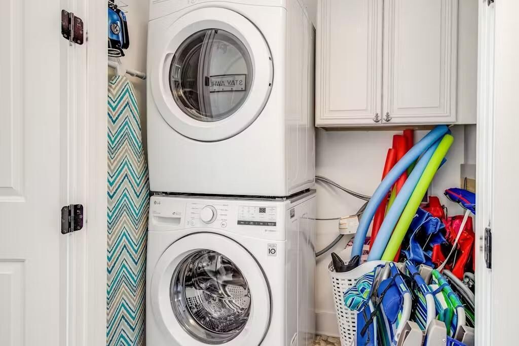 Un espace buanderie comprenant deux machines à laver superposées et un meuble contenant divers objets aux couleurs vives.