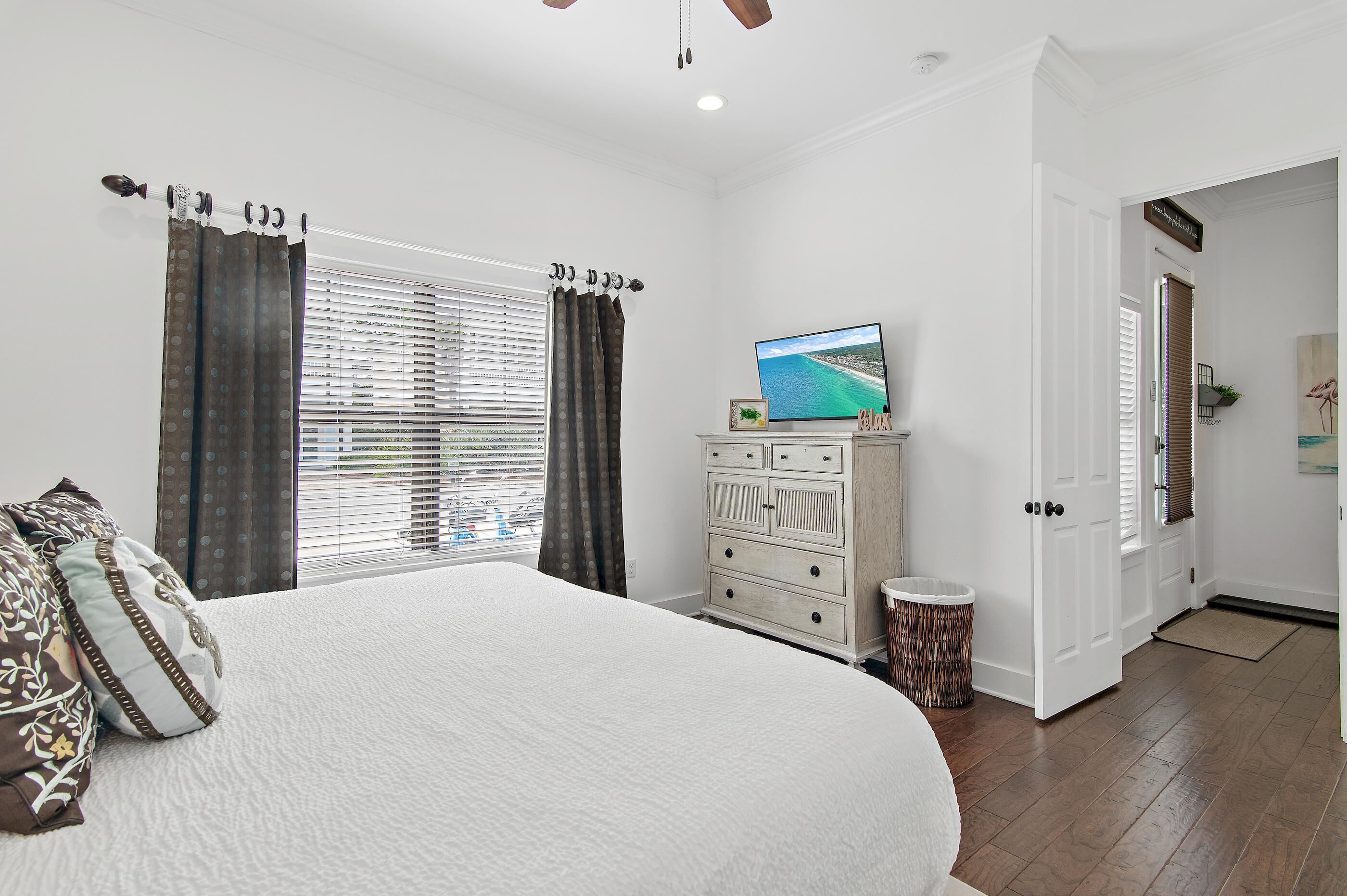 Une chambre avec un grand lit, une commode, un téléviseur et une vue sur l’extérieur par la fenêtre.