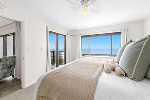 Une chambre avec un grand lit, un ventilateur de plafond et une vue sur l’océan.