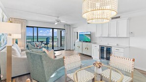 A modern living room with a large window, a chandelier, and a flat-screen TV. - Emerald Towers 305 (Destin)