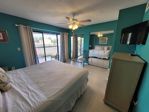 Une chambre d’hôtel comprenant un lit, un ventilateur de plafond, une télévision, une armoire et un balcon avec une chaise et une table.