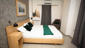 Een moderne hotelkamer met een houten bed, een nachtkastje met een lamp, een spiegel, een klein zithoekje en een airconditioner.