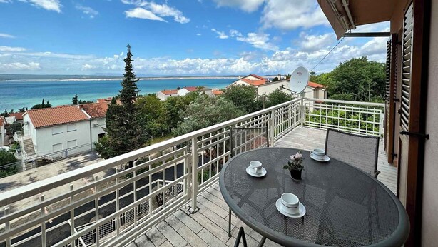 En balkon med et rundt bord, hvide stole og en parabol.