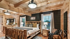 A wooden cabin bedroom with a large bed, a wooden bench, a nightstand, and a mirror. - Newly Renovated! Fishing, Full Game Rm, Hot Tub! (Sevierville)
