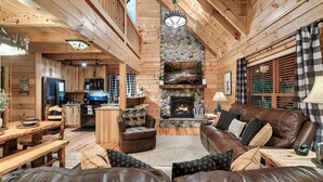 A log cabin interior with a living room, dining area, kitchen, and fireplace. - Newly Renovated! Fishing, Full Game Rm, Hot Tub! (Sevierville)
