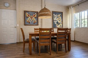 A dining area with a brick wall, wooden dining table, chairs, and two artworks. - El Hogar del Torogoz (Concepción de Ataco)