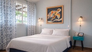 Una camera da letto con un letto, tende, un quadro appeso al muro, lampade sui comodini e un comodino con una sveglia e una cornice.