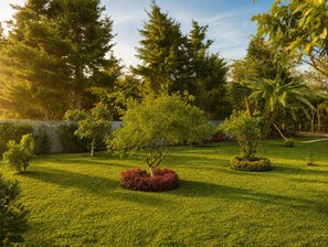 Un jardin bien entretenu, avec divers arbres et arbustes, un ciel dégagé et un mur de pierre en arrière-plan.